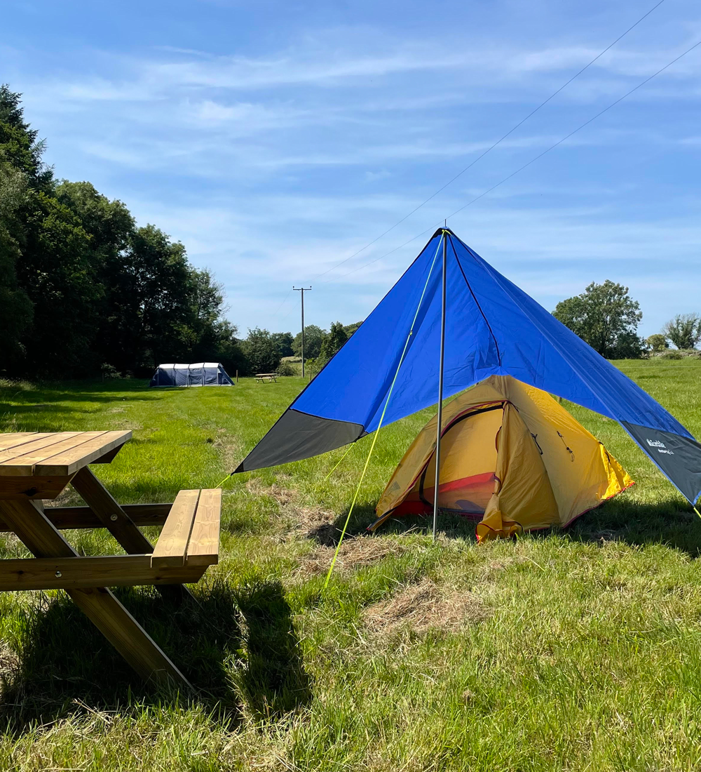 Tent pitched at Coombe Crag campsite with picnic bench and green countryside